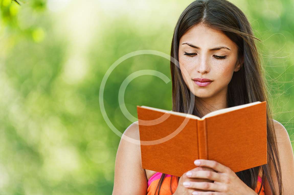 serious young, beautiful girl holding an open book, read background summer green park